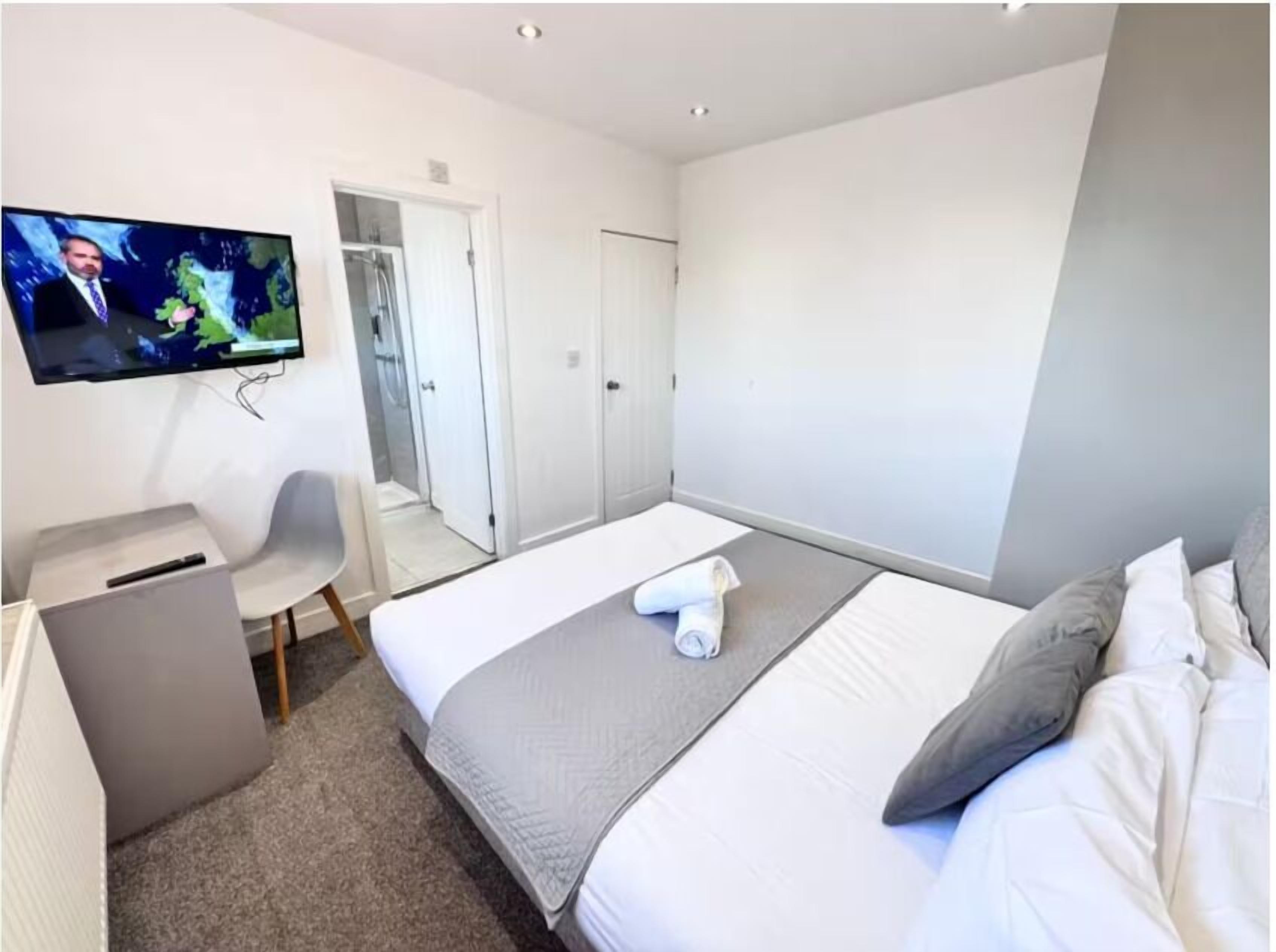 A hotel room with a bed, a desk, a chair, a TV, and a wardrobe.