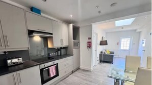 Une cuisine moderne avec des armoires blanches, une cuisinière à gaz et un four à micro-ondes. On y trouve également un coin repas avec une table et des chaises en verre.