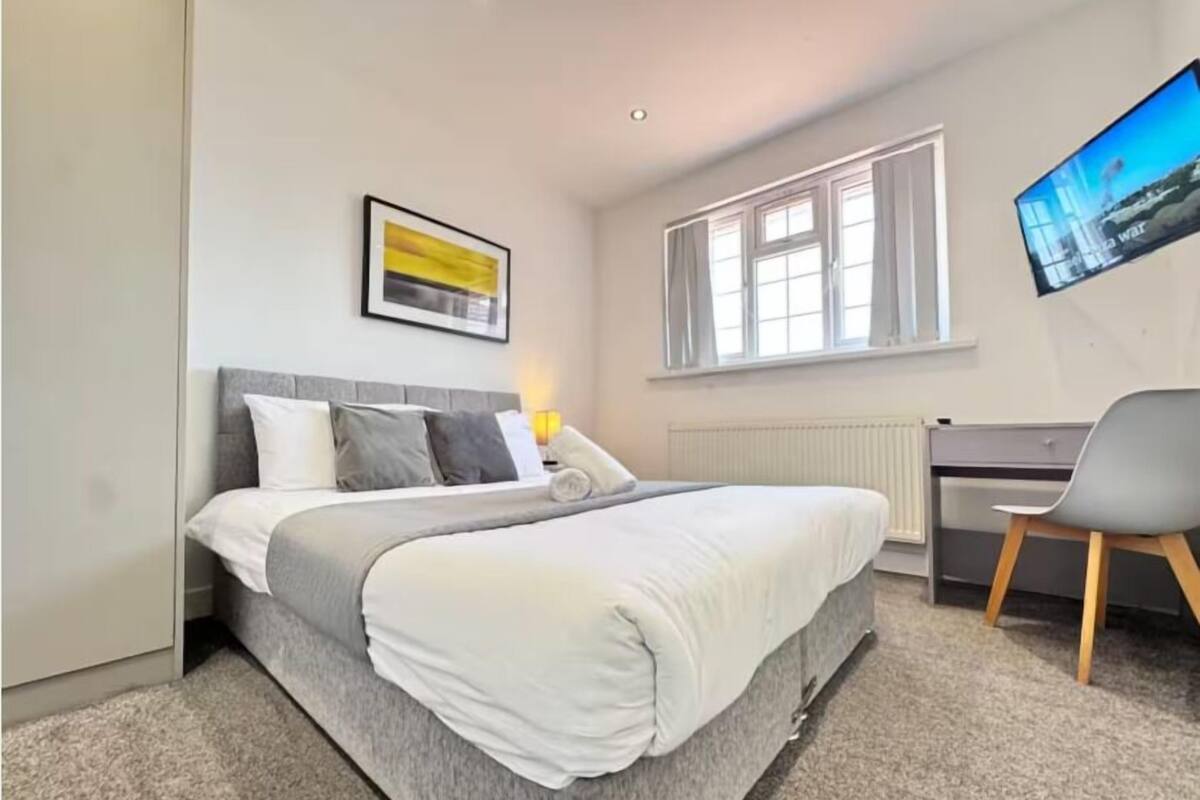 A modern bedroom with a bed, a desk, and a TV.