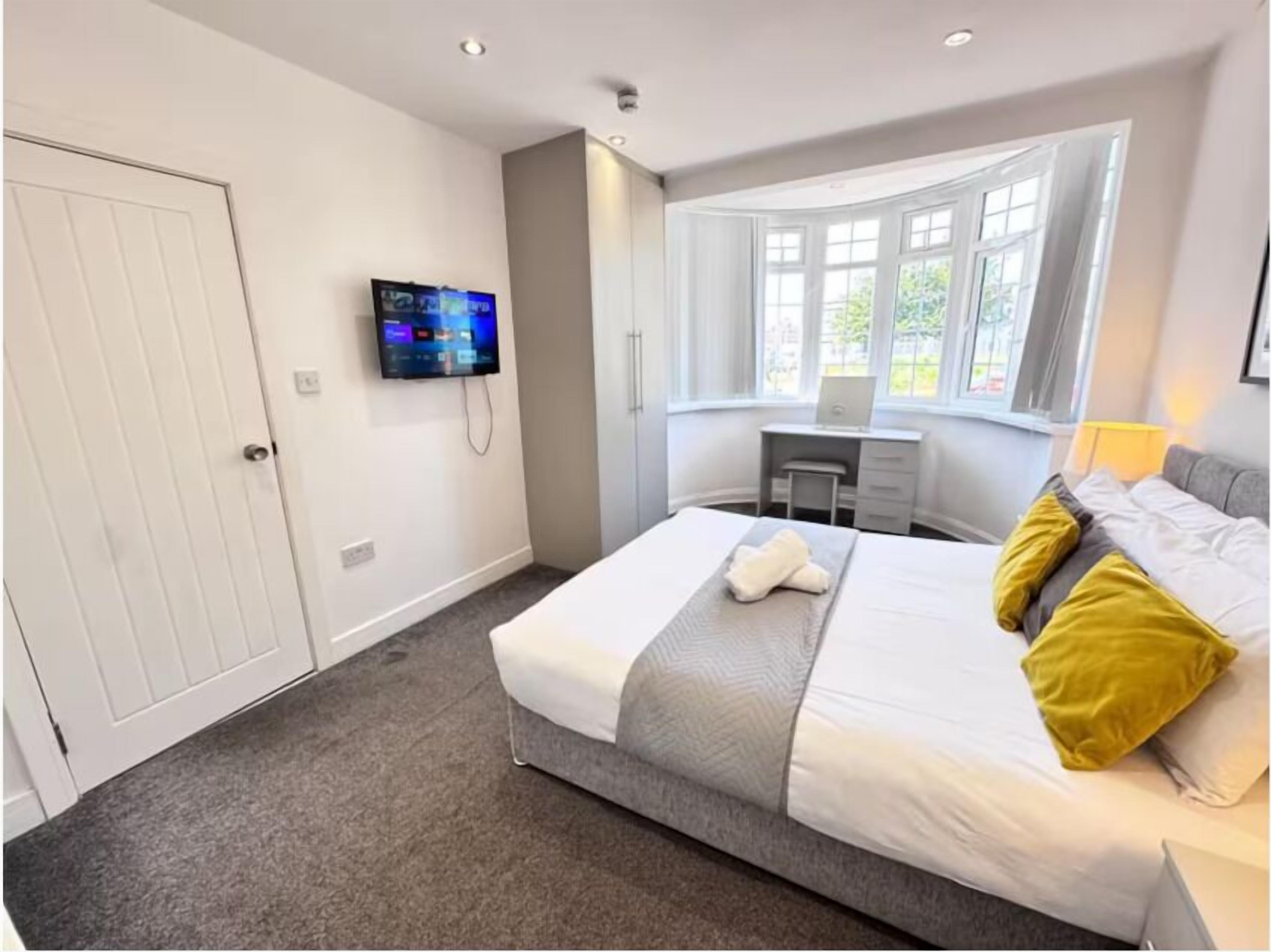 A modern bedroom with a bed, a desk, a TV, and a window.