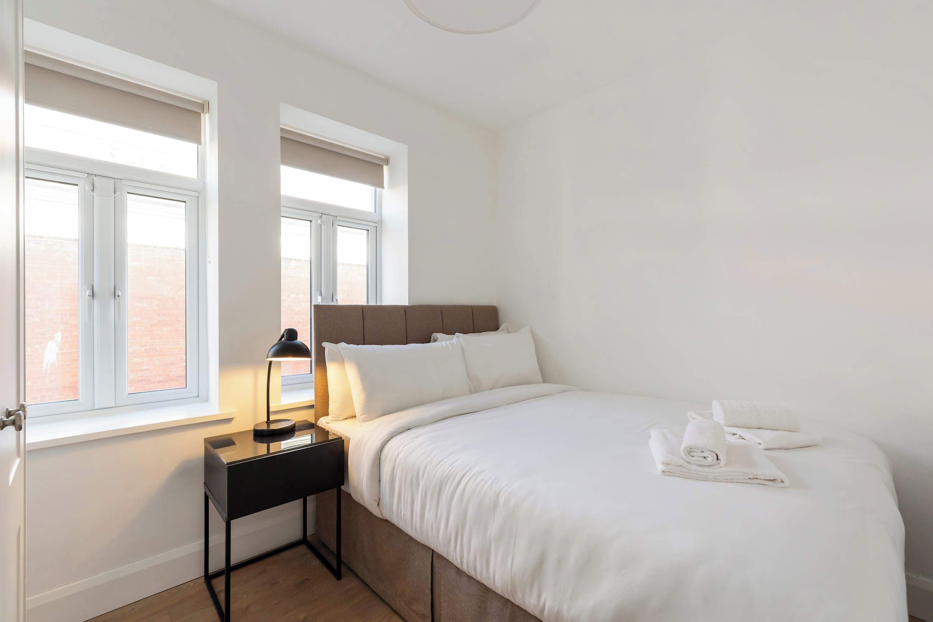 A hotel room with a bed, a nightstand, a lamp, and a window with blinds.