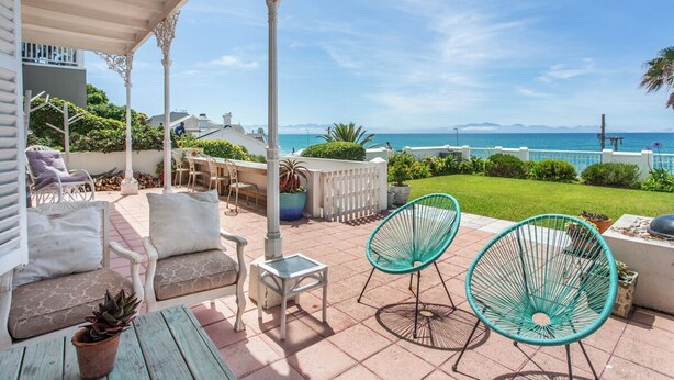 A covered patio with outdoor furniture, a view of the sea, and a well-maintained garden.