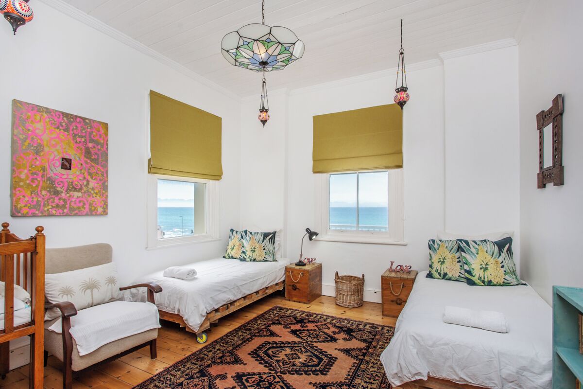 A room with two beds, a chair, a patterned rug, and a large window with a view of the sea.