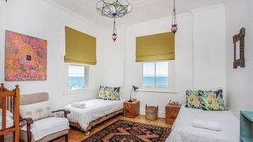 A room with two beds, a chair, a patterned rug, and a large window with a view of the sea.
