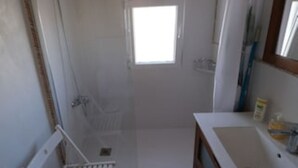 Une petite salle de bain compacte, équipée d’une douche, d’un lavabo et d’une fenêtre.