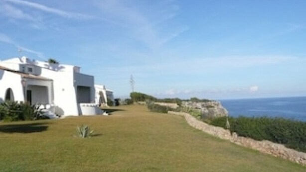 Un bâtiment blanc doté d’un toit plat, d’un mur de soutènement en pierre et offrant une vue sur la mer.
