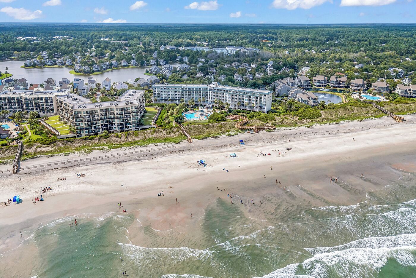 Un hôtel situé sur la côte, composé de plusieurs bâtiments, avec une plage de sable et un lac en arrière-plan.