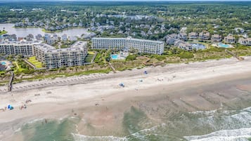 Un hôtel situé sur la côte, composé de plusieurs bâtiments, avec une plage de sable et un lac en arrière-plan.