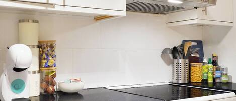 A kitchen with a stove, a coffee maker, and various kitchen utensils and ingredients on the counter.