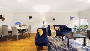 A modern living room with a blue sofa, a dining table with chairs, a coffee table, and a floor lamp. - Lux 3-Bed 3-Bath Apt, Terrace, Underground Parking (London)