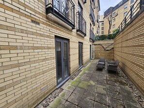 A courtyard with a brick wall, a door, and a seating area with chairs. - Lux 3-Bed 3-Bath Apt, Terrace, Underground Parking (London)