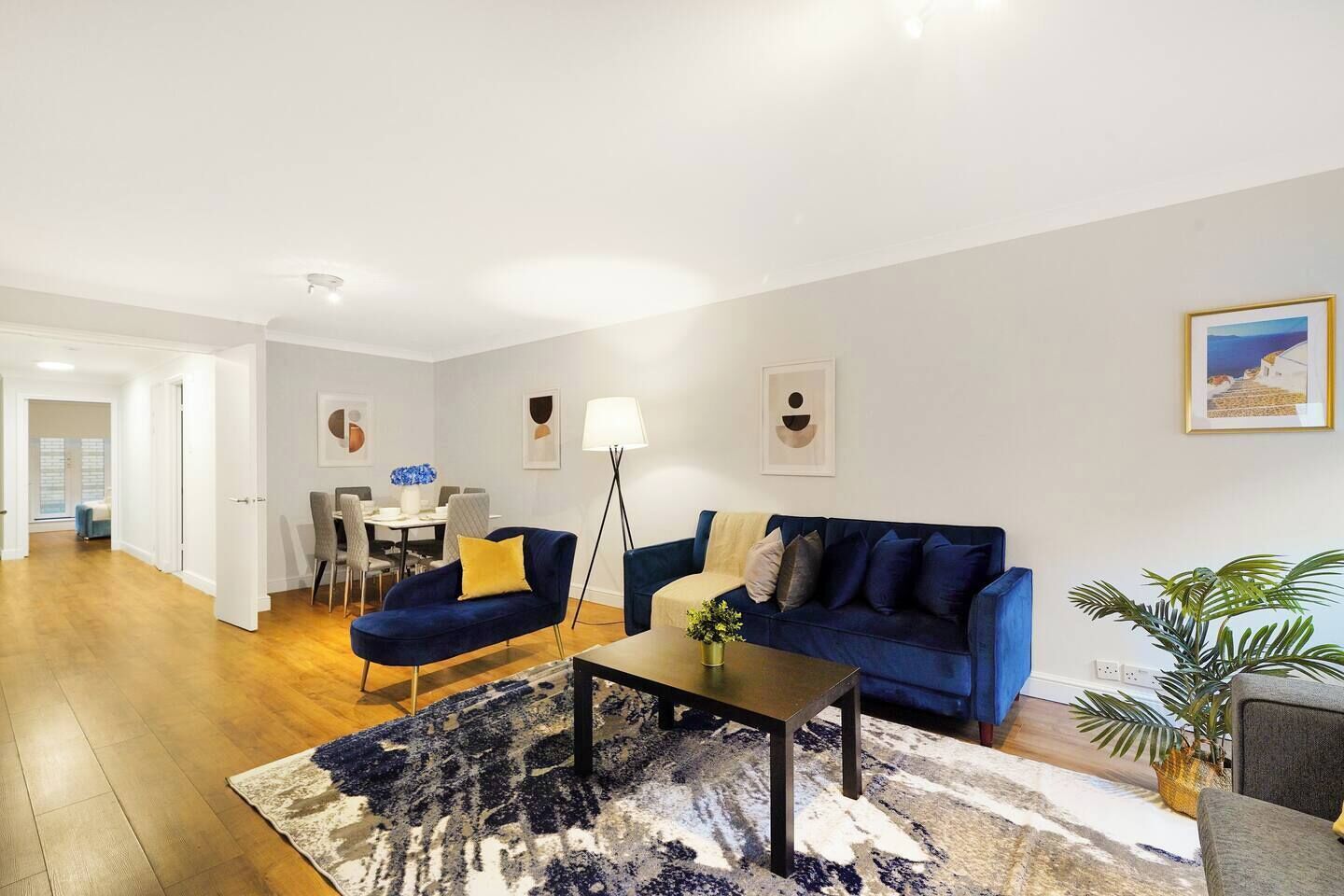 A modern living room with a blue sofa, a coffee table, and a dining area in the background.