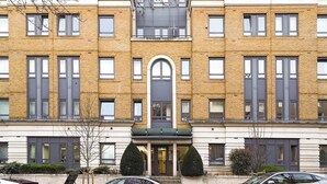 A multi-story building with a central arched entrance, a flat facade, and a row of windows on each floor. - Lux 3-Bed 3-Bath Apt, Terrace, Underground Parking (London)