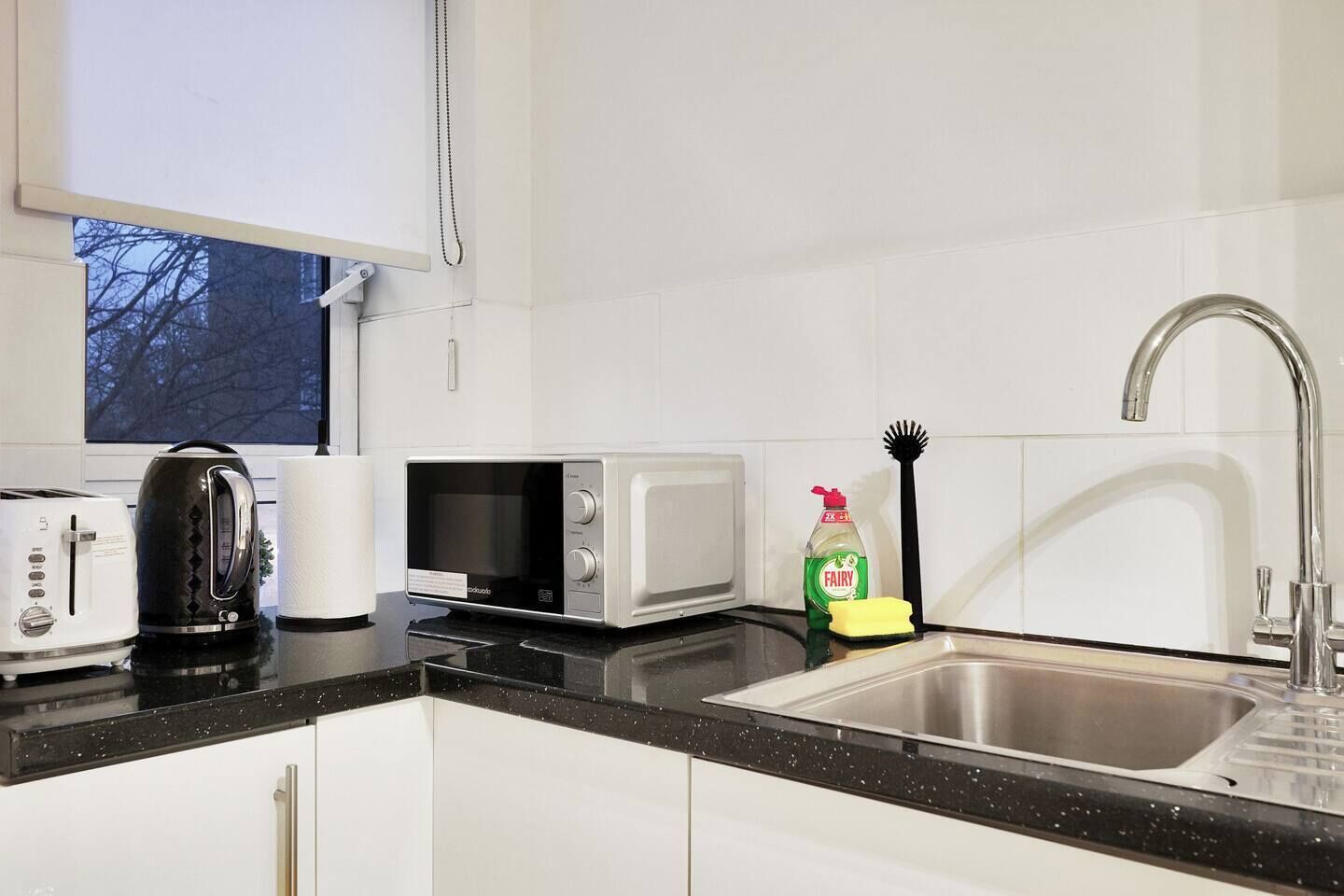 A modern kitchen with a toaster, kettle, microwave, and a sink with a faucet.