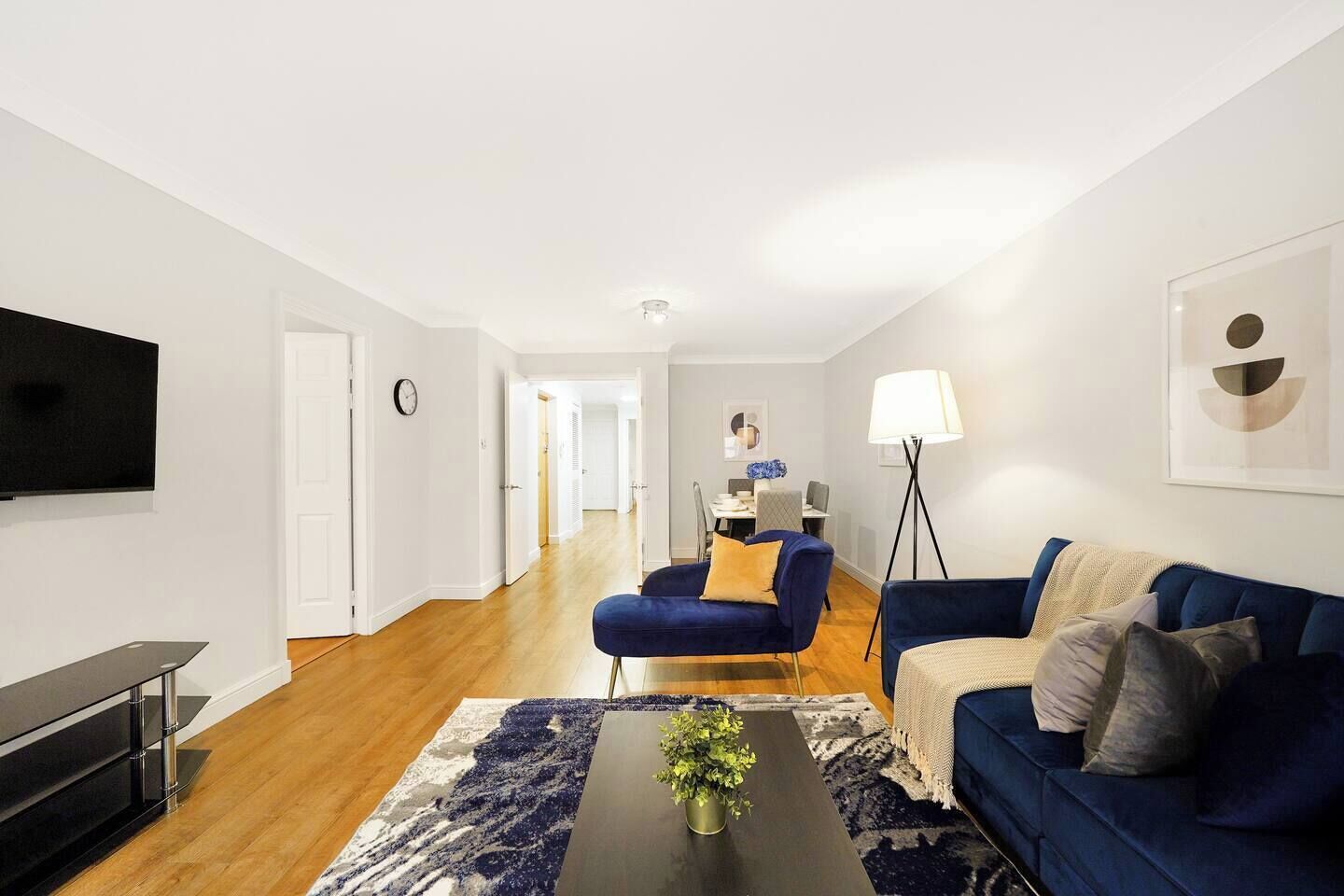 A modern living room with a blue sofa, a coffee table with a plant, a TV, and a lamp.