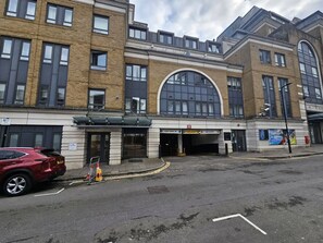 A building with a large arched entrance, a red car parked in front, and a sign indicating a car park. - Lux 3-Bed 3-Bath Apt, Terrace, Underground Parking (London)