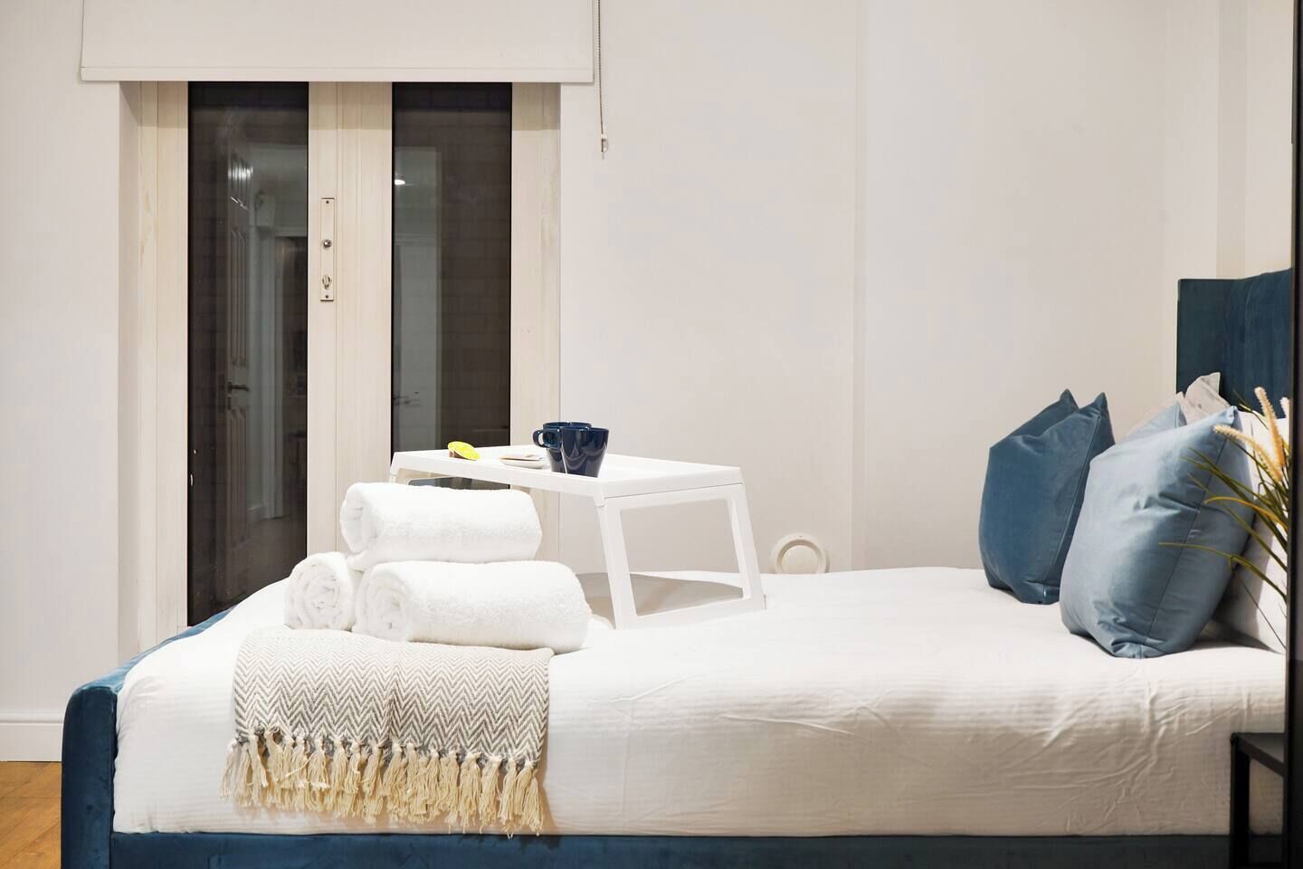 Un dormitorio con cama, mesita de noche, ventana y puerta.