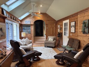 A cozy cabin interior with a loft bedroom, wooden walls, a ceiling fan, a fireplace, and a dining area. - Pitcher Perfect Truly the perfect  LAKEFRONT Maine getaway (Lincolnville)