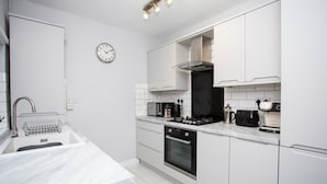 Une cuisine moderne avec des meubles blancs, un évier en acier inoxydable, un four encastré et une horloge au mur.