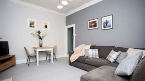 Un salon avec un canapé gris, une petite table et un téléviseur.