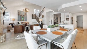 Uma sala de estar espaçosa com uma grande mesa de jantar, uma escada e uma cozinha ao fundo.