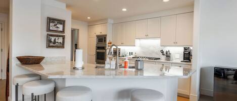 A modern kitchen with a central island, bar stools, and a stainless steel dishwasher.