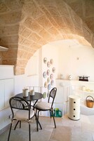 A stone archway leading to a kitchen with a round table, two chairs, and a wall decorated with plates.