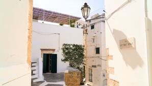 Egy keskeny utca, melyben egy kőből épített lépcső vezet egy épület bejáratához, egy cserépben lévő növény és egy közvilágítási lámpa található.