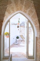 An arched doorway leading to a balcony with a tiled floor, a chair, and potted plants.