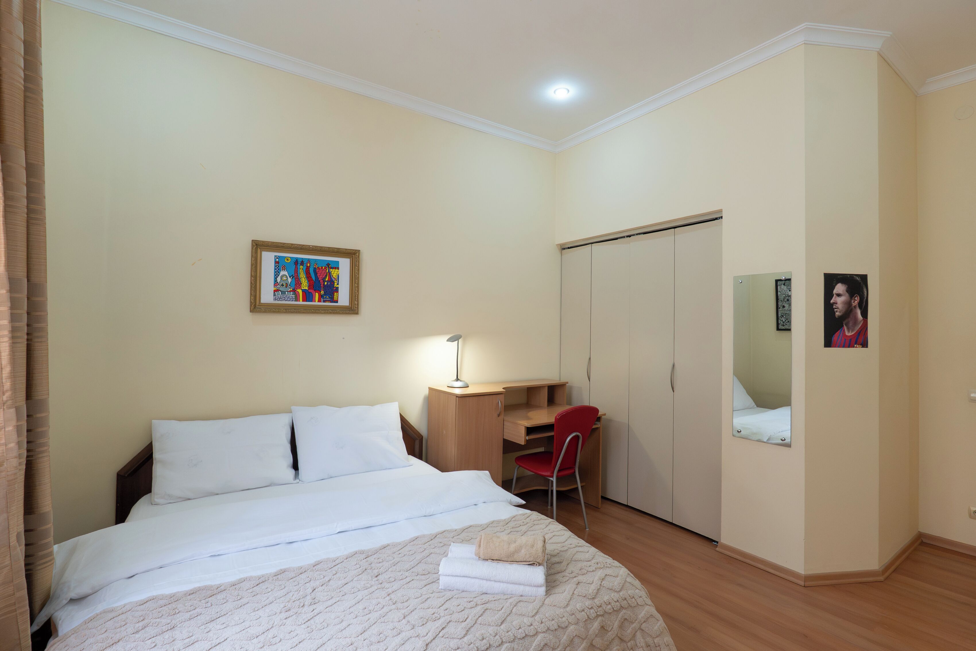 A bedroom with a bed, a desk, a chair, a wardrobe, and a framed picture on the wall.