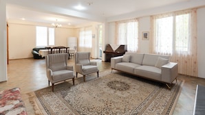 En rummelig stue med en beige sofa, to lænestole, et sofabord og et klaver.