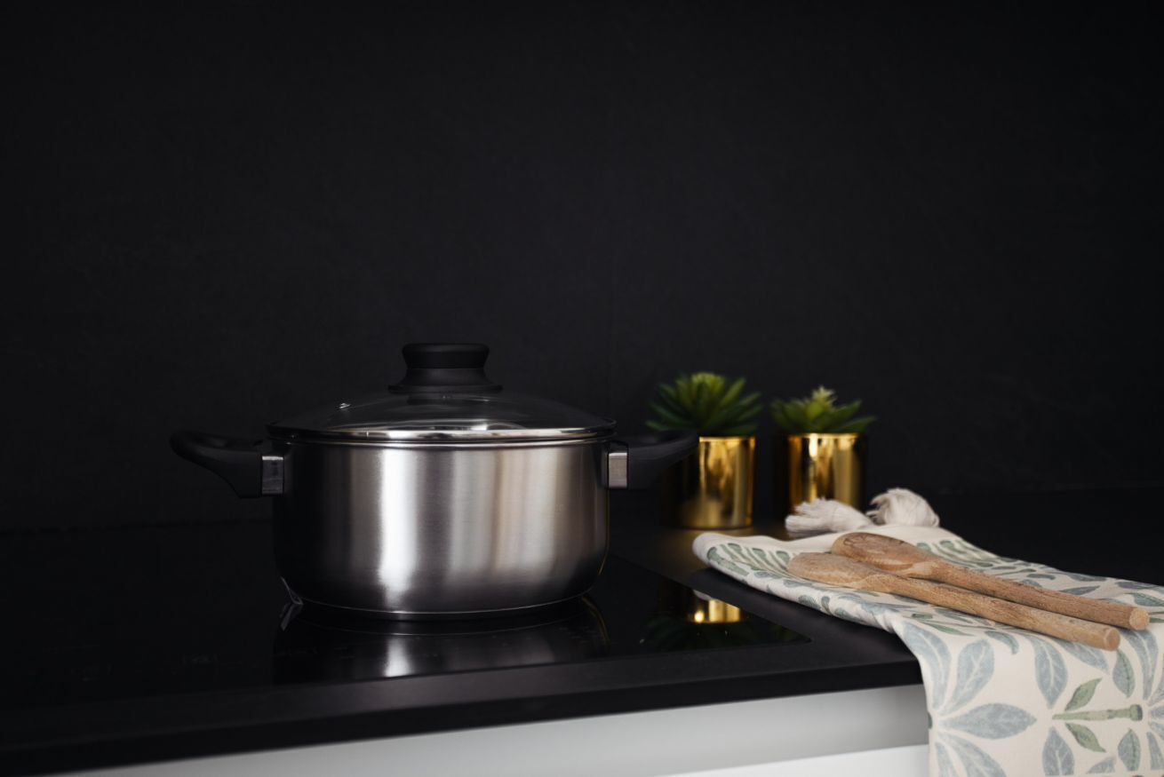 Une casserole en acier inoxydable sur un comptoir noir, avec une plante et un tissu à proximité.