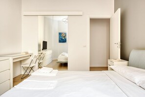 Une chambre d’hôtel moderne équipée d’un lit, d’un bureau, d’une chaise, d’une petite table et d’une porte donnant sur une autre pièce.