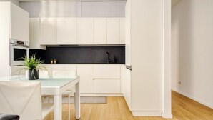 A modern kitchen with white cabinetry, a black countertop, and a dining area with a glass table and chairs. - Hostmate - Milano - Donatello - Città Studi (Milano)