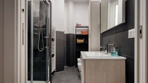 A modern bathroom with a glass shower enclosure, a white sink, and a wooden vanity. - Hostmate - Milano - Donatello - Città Studi (Milano)