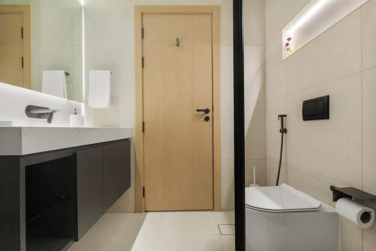 Une salle de bain moderne avec une porte en bois, un lavabo blanc, des toilettes et une douche.