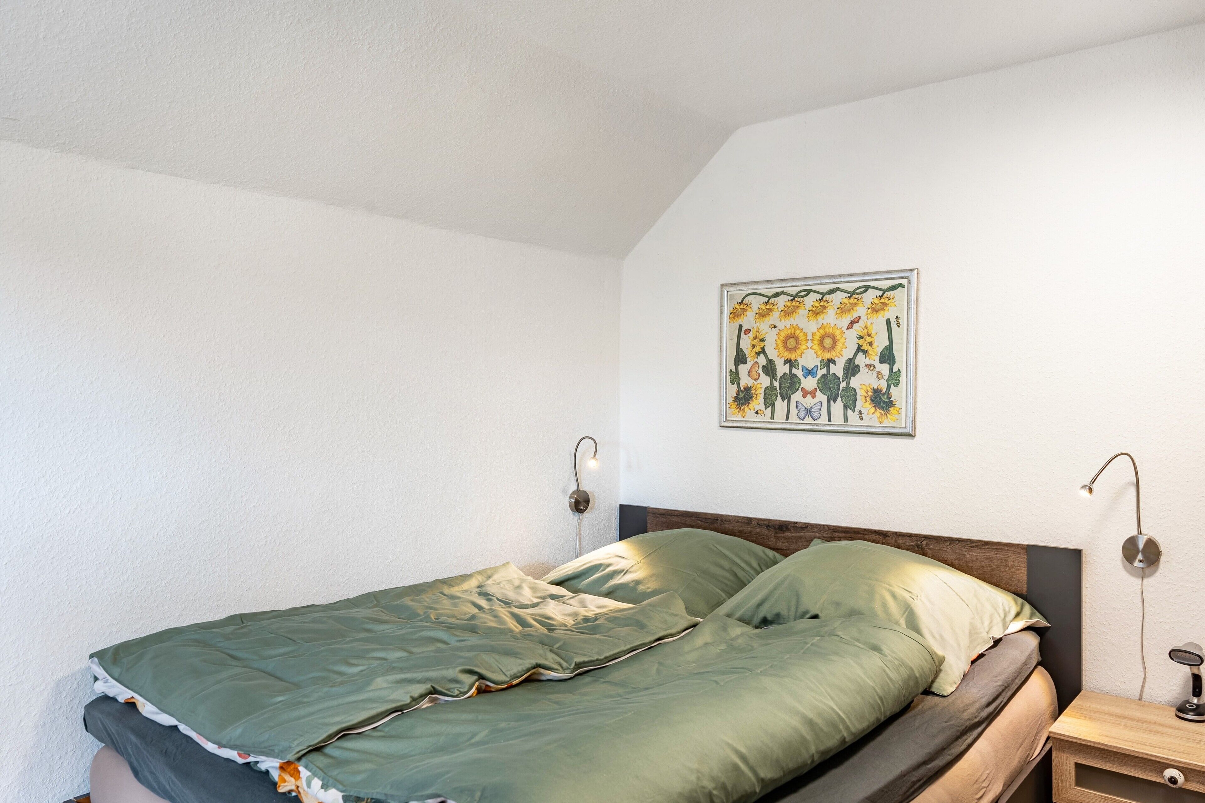 Ein Schlafzimmer mit einem Bett, einer Wandlampe und einem gerahmten Pflanzenbild.