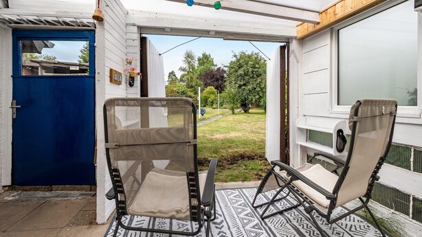 Un'area patio coperta con due poltrone in vimini, un tappeto decorato e vista su un giardino.