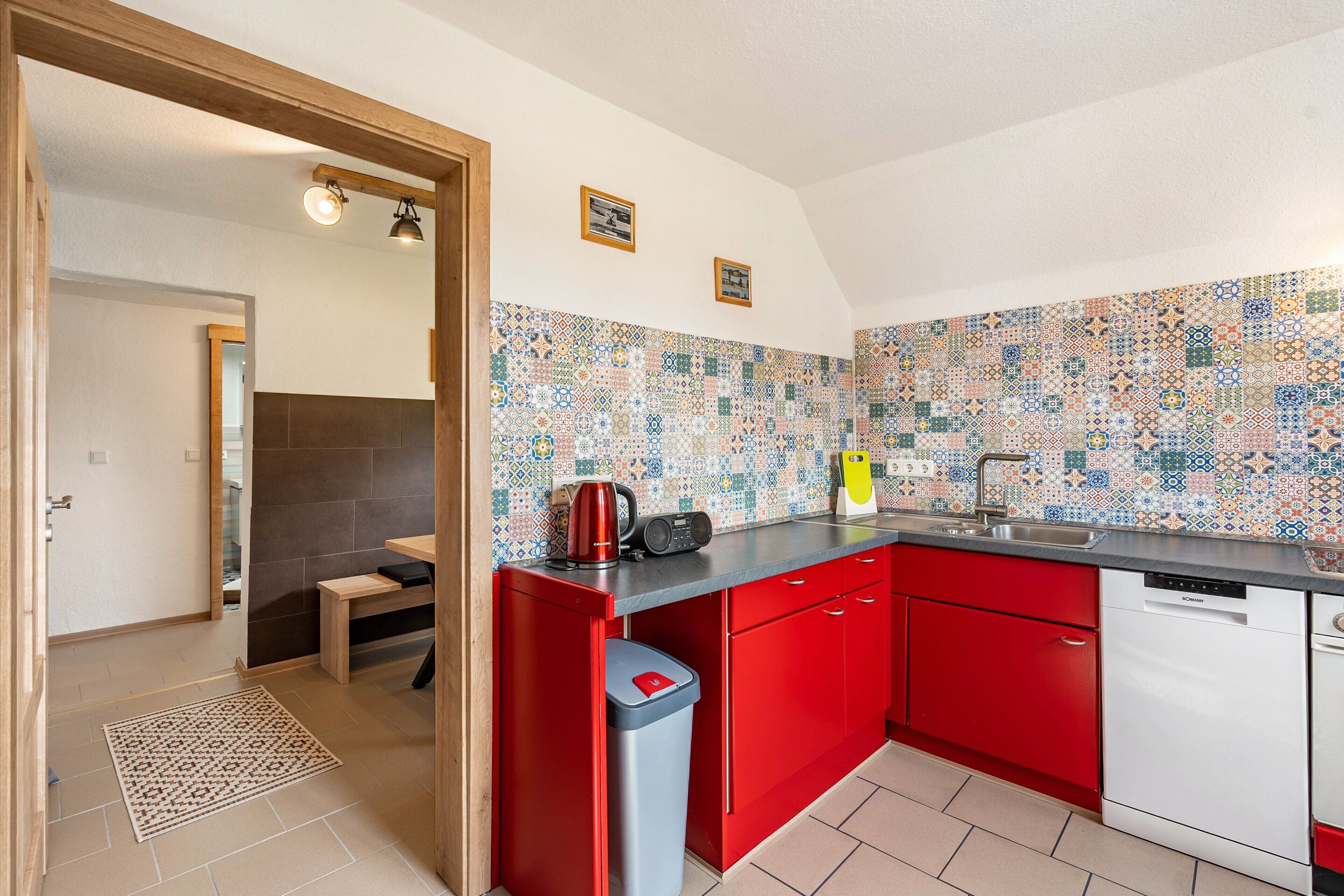 A kitchen with red cabinets, a black countertop, and a tiled backsplash.