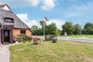 A house with a thatched roof, a flag, and a fenced yard with potted plants. - Holiday Home 'Reethaus Kälberstieg' with Lake View, Private Terrace and Wi-Fi (Grebin)