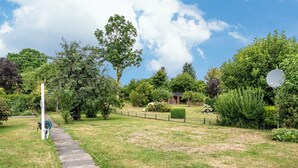Un vialetto che si snoda attraverso un giardino con diversi alberi e arbusti, una recinzione e un pannello solare.