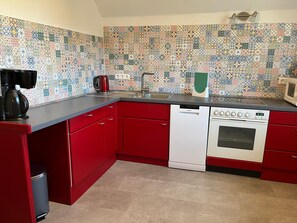 A kitchen with red cabinets, a white dishwasher, a microwave, and a coffee maker. - Holiday Home 'Reethaus Kälberstieg' with Lake View, Private Terrace and Wi-Fi (Grebin)