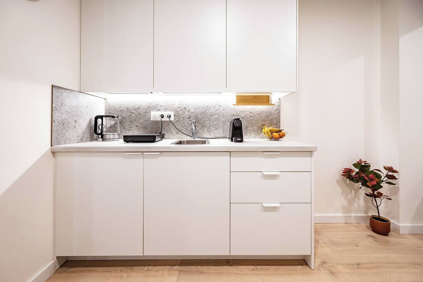 A compact kitchen with a countertop, a sink, a coffee maker, a kettle, and a fruit bowl.