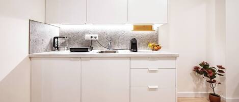 A compact kitchen with a countertop, a sink, a coffee maker, a kettle, and a fruit bowl.