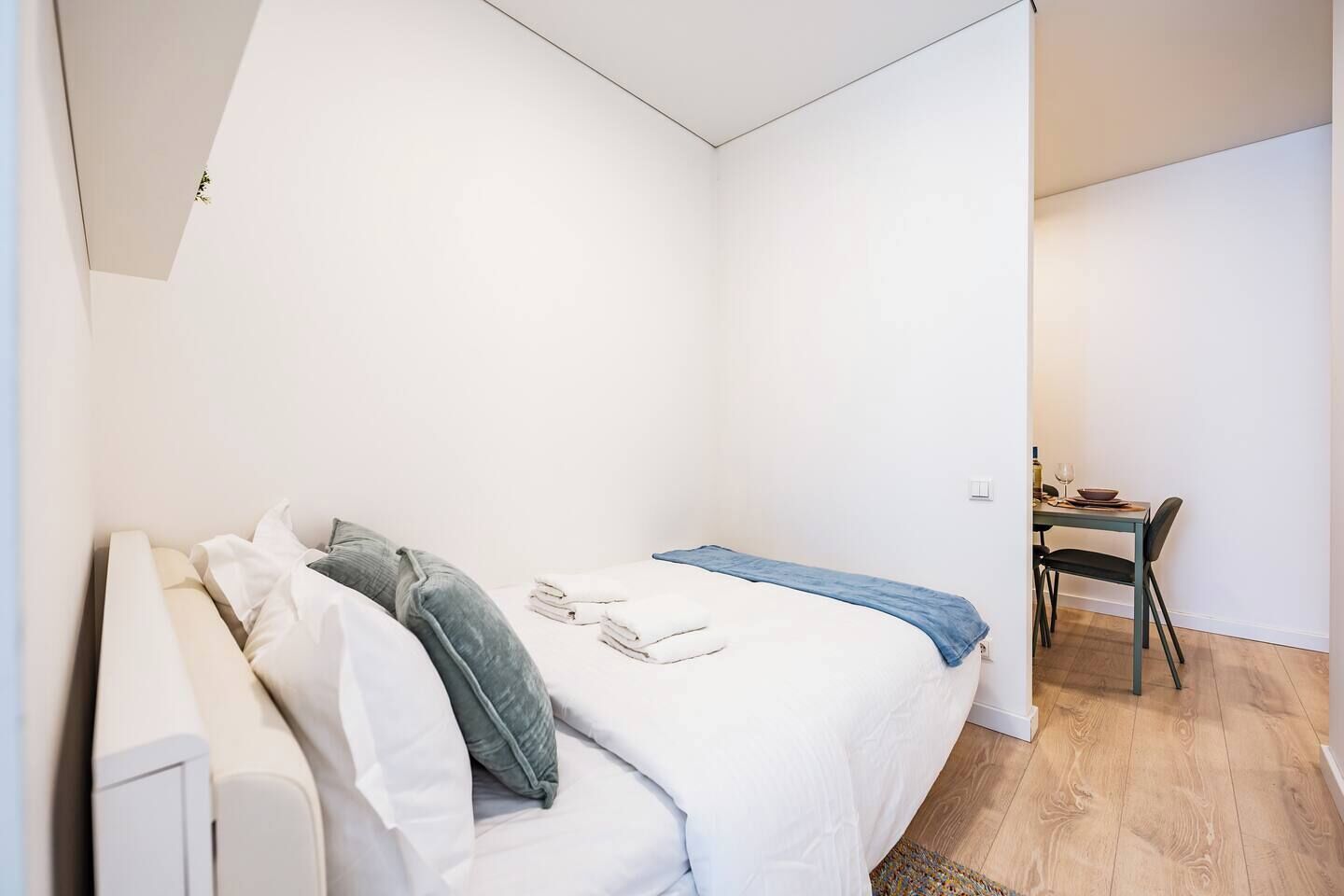A bedroom with a bed, pillows, a desk with a chair, and a dining table with chairs.