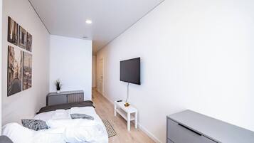 A modern bedroom with a bed, a flat-screen TV mounted on the wall, and a small white table with a plant.