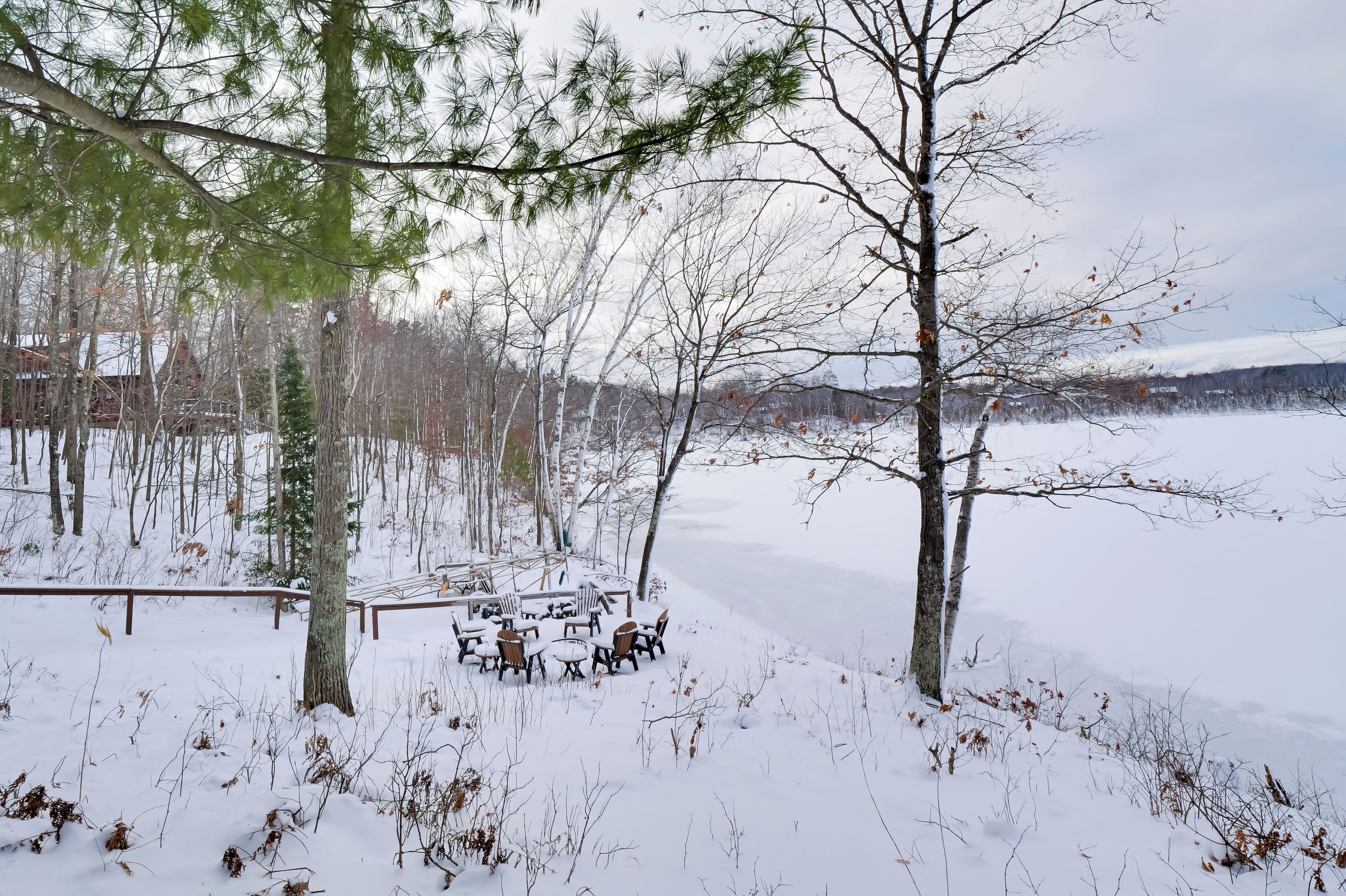 A snow-covered outdoor area with a table and chairs, surrounded by trees and a fence.