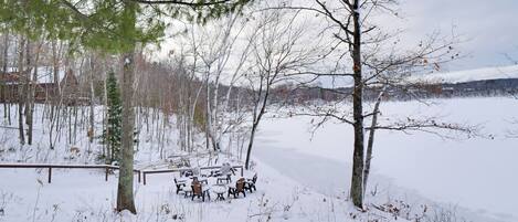 A snow-covered outdoor area with a table and chairs, surrounded by trees and a fence.