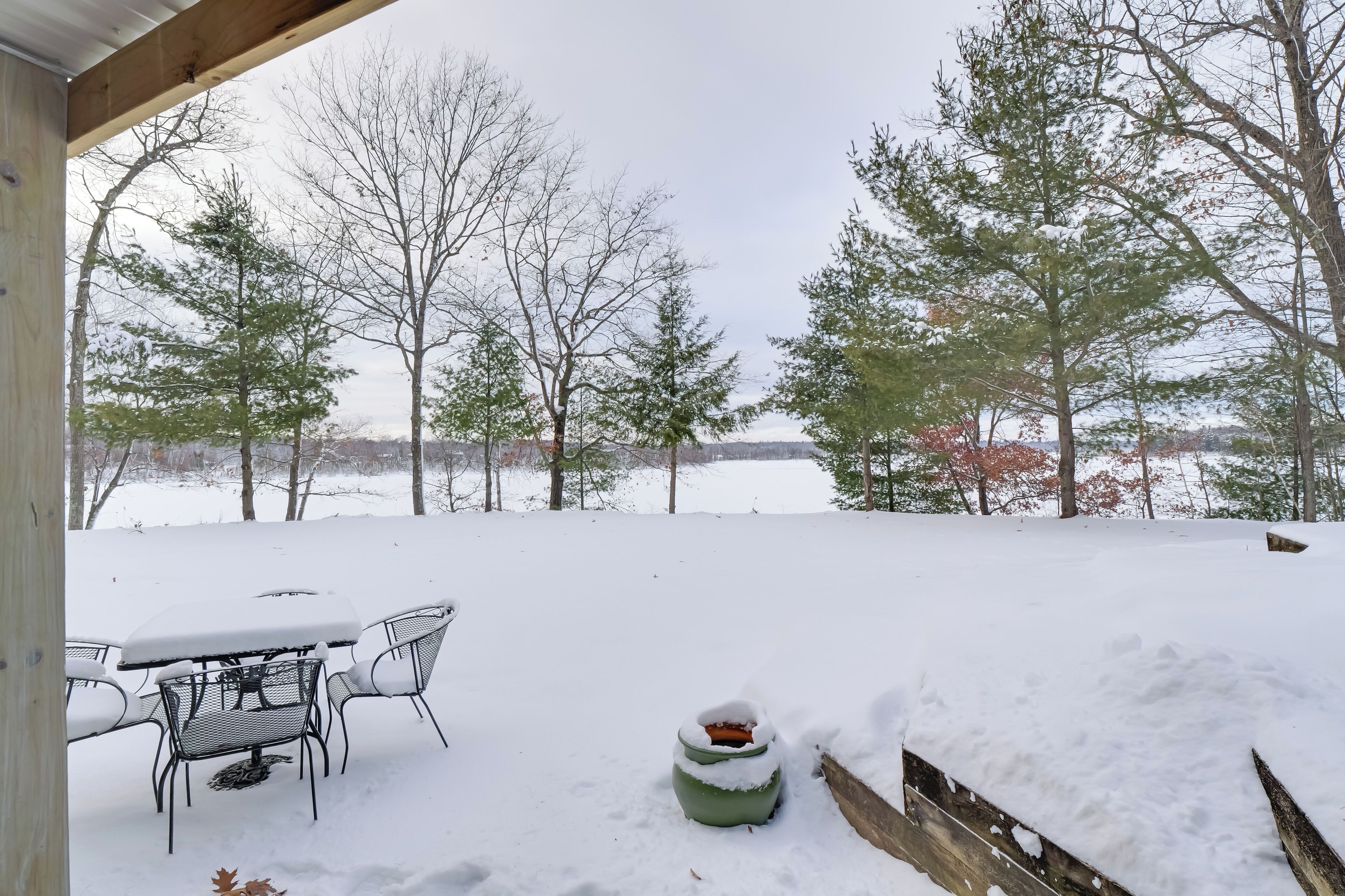 A snow-covered patio with a table and chairs, a green planter, and a wooden fence.