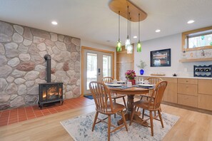 A dining area with a stone wall, a wood-burning stove, and a wooden dining table with chairs. - Lakeside Retreat in Hayward: Pet Friendly! (Hayward)